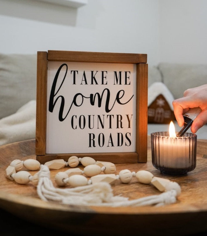 Country Roads Take me Home Framed sign next to a candle on a coffee table